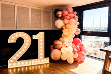 Load image into Gallery viewer, A marquee light sign with the number 21 in white and pink balloons, set up indoors with balloons spelling out '21' and decorative lights.
