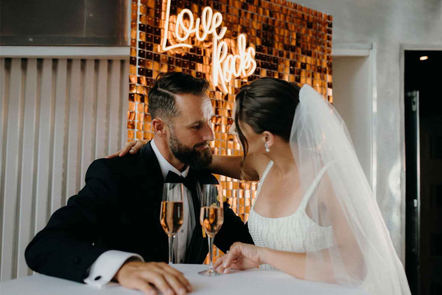 Wedding photo backdrop featuring a copper shimmer wall and Love Rocks neon sign