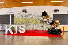 Load image into Gallery viewer, Corporate event backdrop featuring a white gold shimmer wall with balloons, marquee lights, and red carpet entrance.