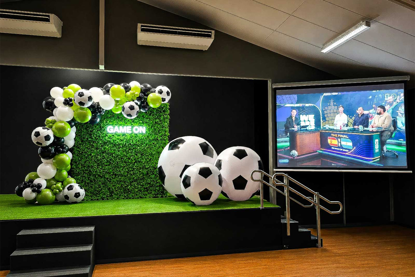 Soccer backdrop setup with organic green, black and white balloon garland, hedge wall, Game On neon sign and giant soccer ball props for World Cup parties and soccer-themed events in Auckland.