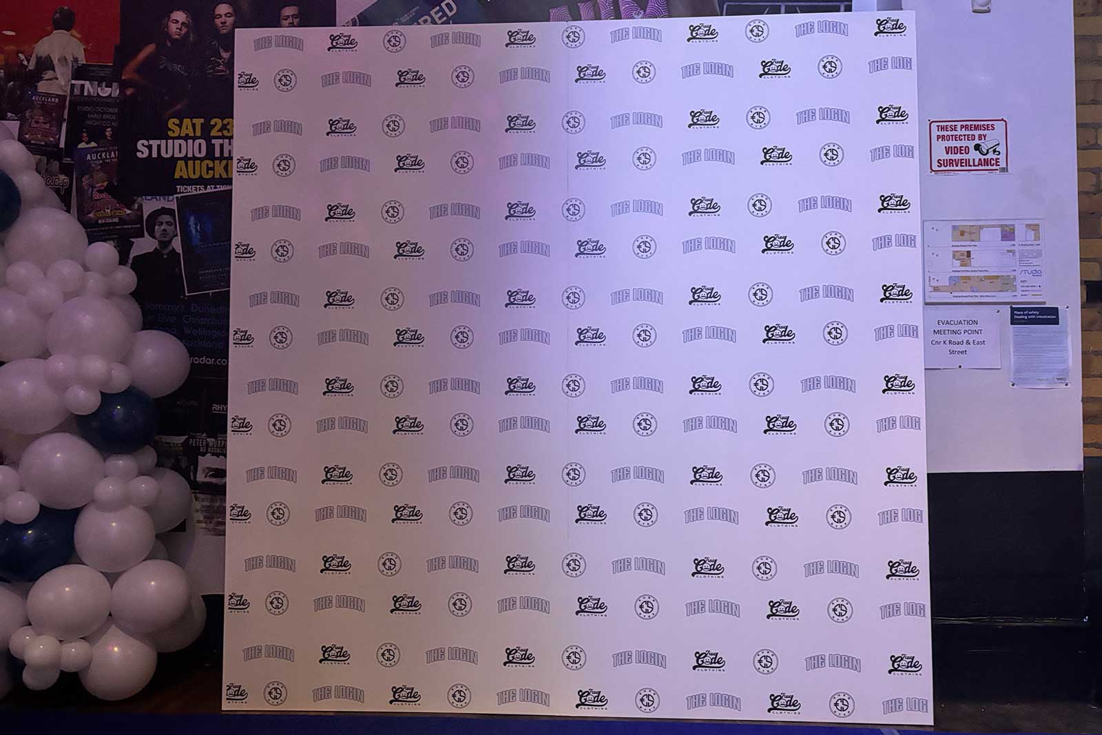 White step and repeat banner with logos on a stand, surrounded by balloons and posters. Media Wall