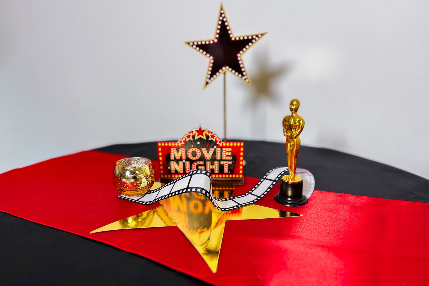 Decorative centrepiece setup with movie night sign, star, and Oscar statue on a red and black surface.