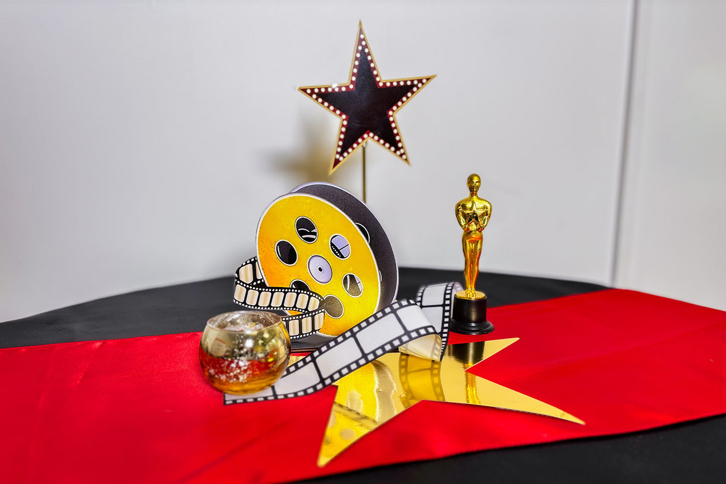 Decorative centrepiece setup with movie-themed items including a star, film reel, and Oscar statue on a red and black surface.