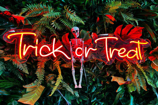 Neon 'Trick or Treat' sign with a skeleton surrounded by foliage