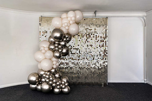 A balloon garland featuring balloons in white and white gold shades, arranged in front of a reflective, grid-patterned backdrop.