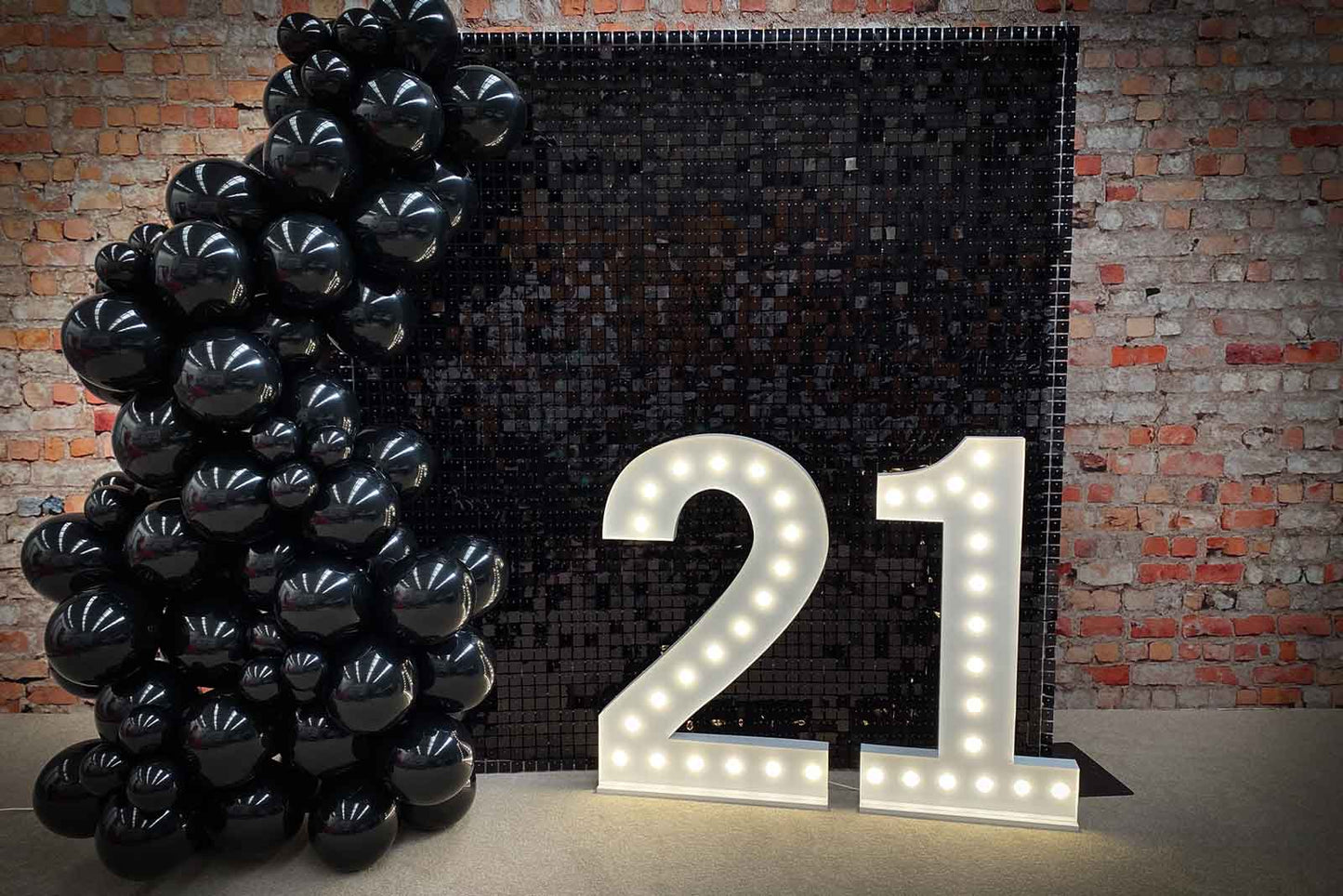 Black shimmer wall backdrop with illuminated 21 marquee lights for a 21st birthday celebration in New Zealand