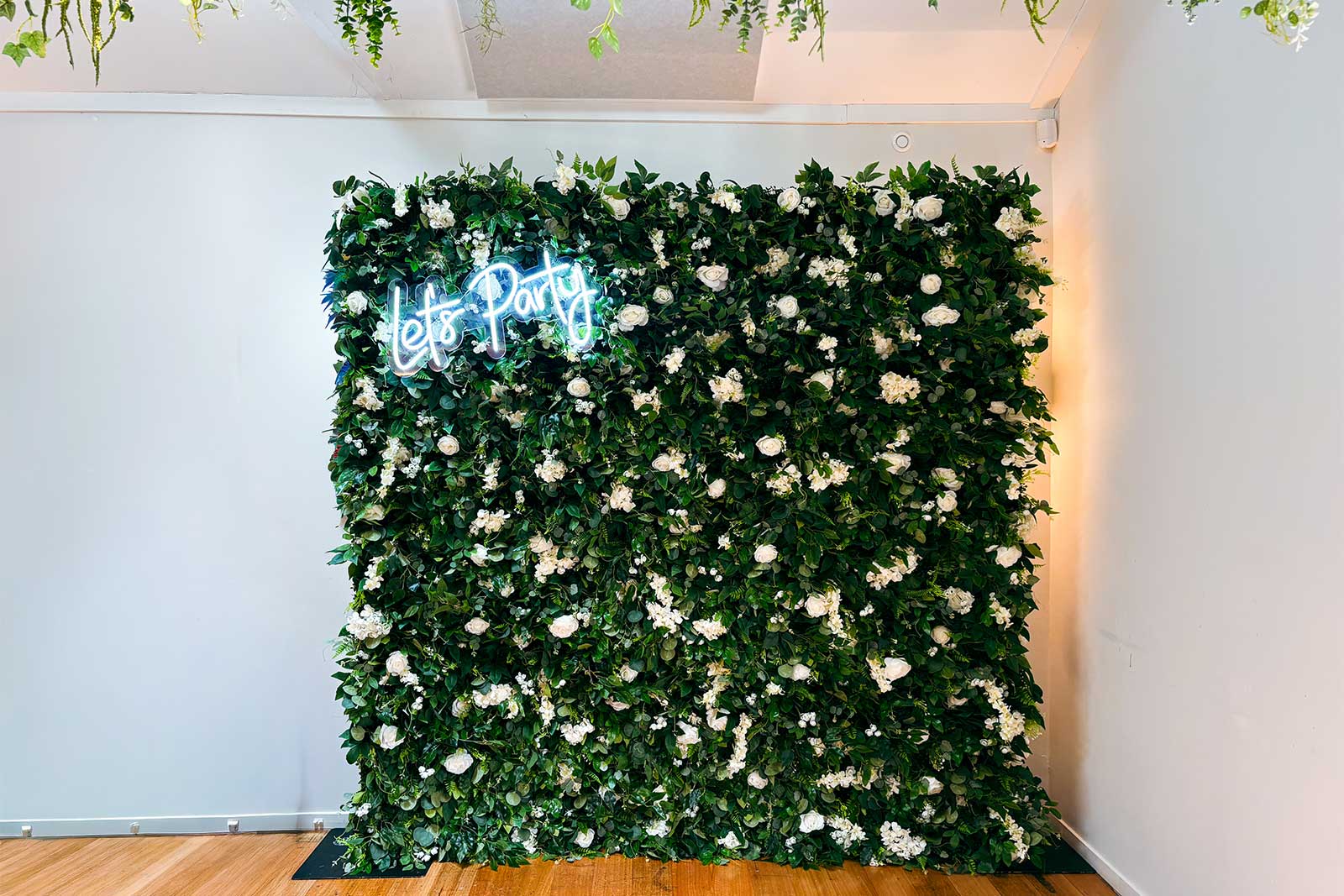 Flower wall styled with “Let’s Party” neon sign for birthday and celebration hire in Auckland.