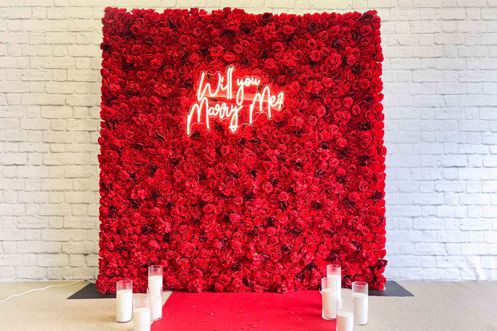 Red flower wall backdrop with “Will You Marry Me” neon sign for proposal and engagement events in Auckland NZ