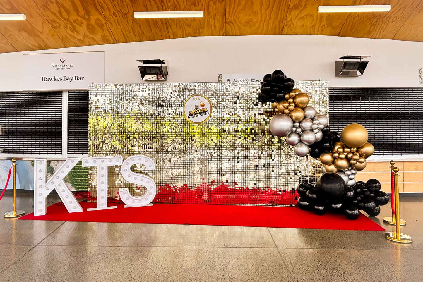 Corporate event backdrop featuring a white gold shimmer wall with balloons, marquee lights, and red carpet entrance.