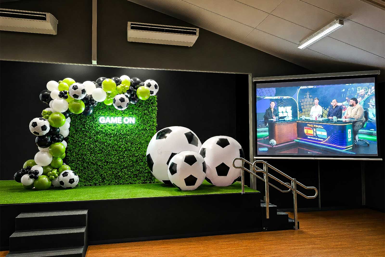 Soccer backdrop setup with organic green, black and white balloon garland, hedge wall, Game On neon sign and giant soccer ball props for World Cup parties and soccer-themed events in Auckland.