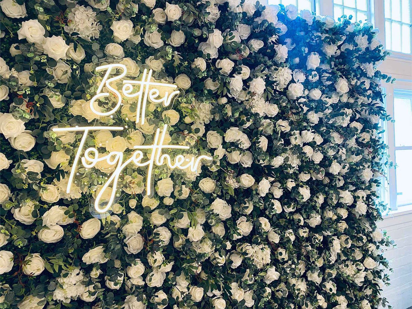 Lush floral wedding wall with glowing "Better Together" neon sign for ceremony décor