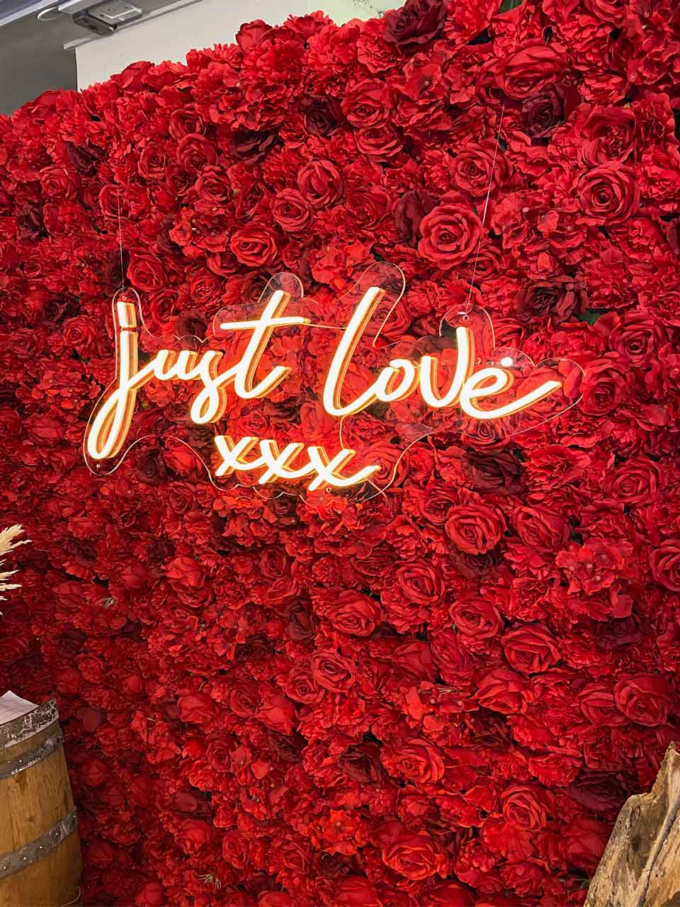 Red flower wall backdrop with “Just Love” neon sign for weddings, engagements, and romantic events in Auckland NZ